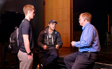 Professor having conversation with two students in the Denault Auditorium