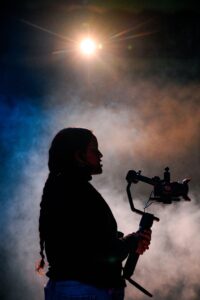 student holding a camera with light in background.