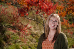 A photo of her in front of a tree. The leaves are shades of red and green