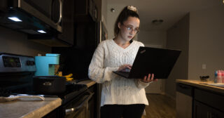 A woman uses a laptop computer in a kitchen.