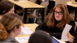 A woman professor speaks with students at a desk