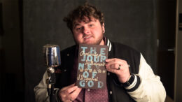 A man in a varsity jacket holds a book with the words 