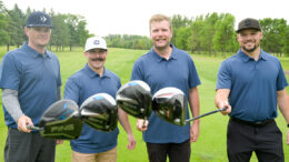 Four golfers touch their clubs together and smile for the camera.