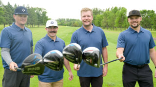 Four golfers touch their clubs together and smile for the camera.