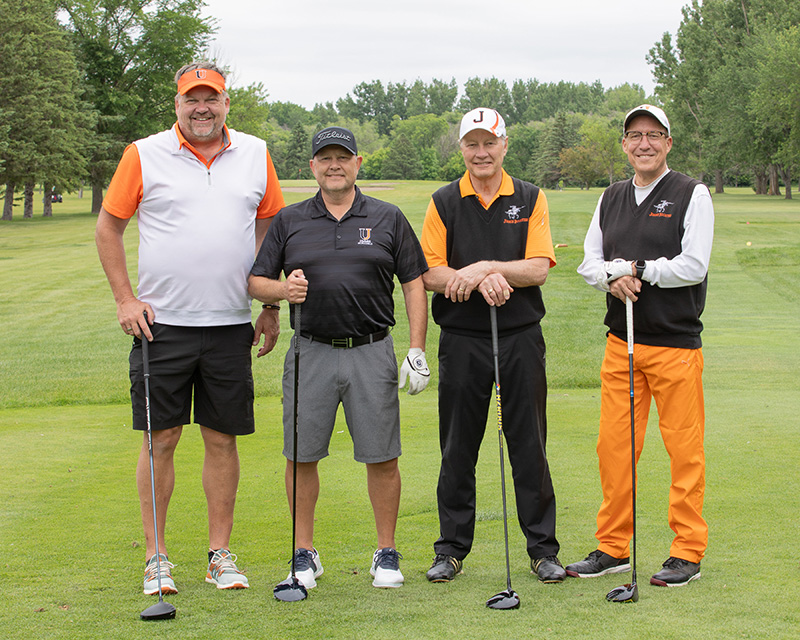 Four golfers in orange, black, and white clothes pose for a portrait. 
