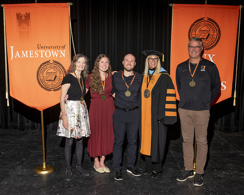 Five people pose for a portrait in front of two orange banners.
