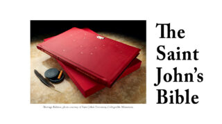 Two volumes of the Saint John's Bible in the form of large red books on a table with an inkwell and quill beside them.
