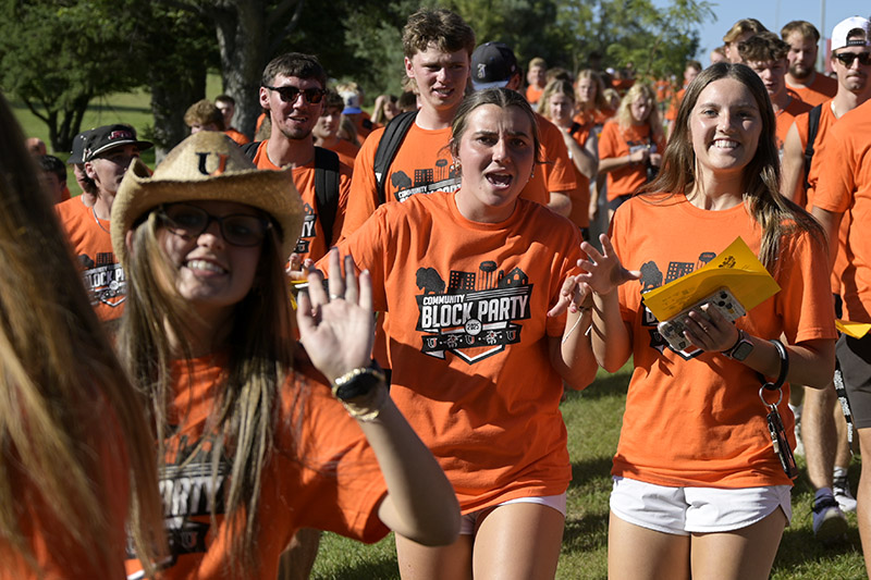 A crowd of college students wearing orange shirts smile for a photo while walking down a hill. 