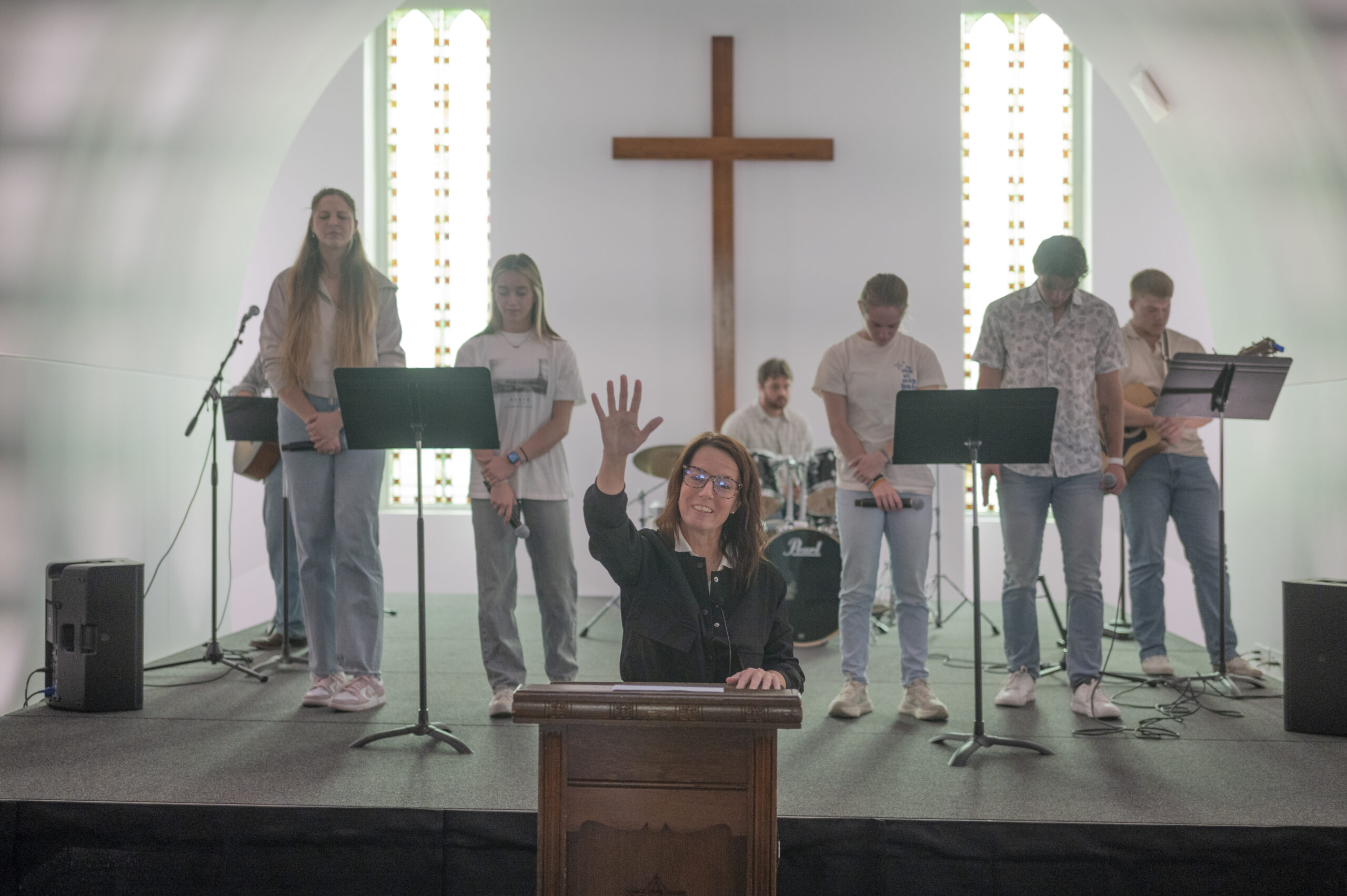 Kirstie Dobson, Director of Campus Ministry and Pastoral Care Coordinator, leads a worship service at the University of Jamestown with a student worship team on stage behind her.