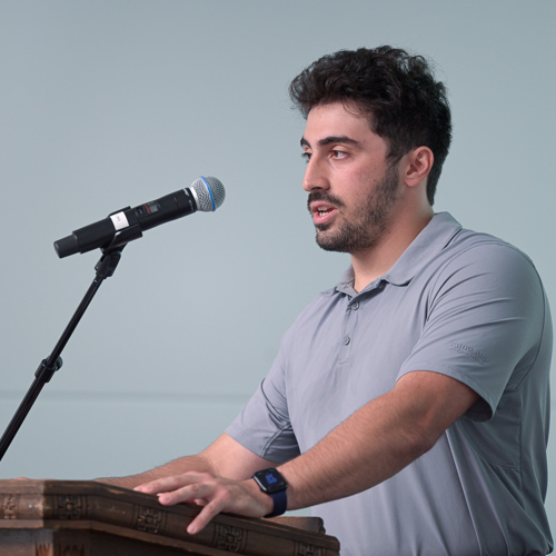 A man in a grey polo shirt speaks into a microphone. 