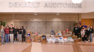 A group of young people stand on opposite sides of a large group of boxes and bags of food.