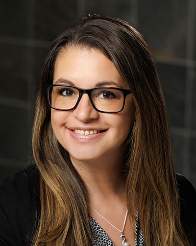 A woman with brown hair and black glasses smiles.