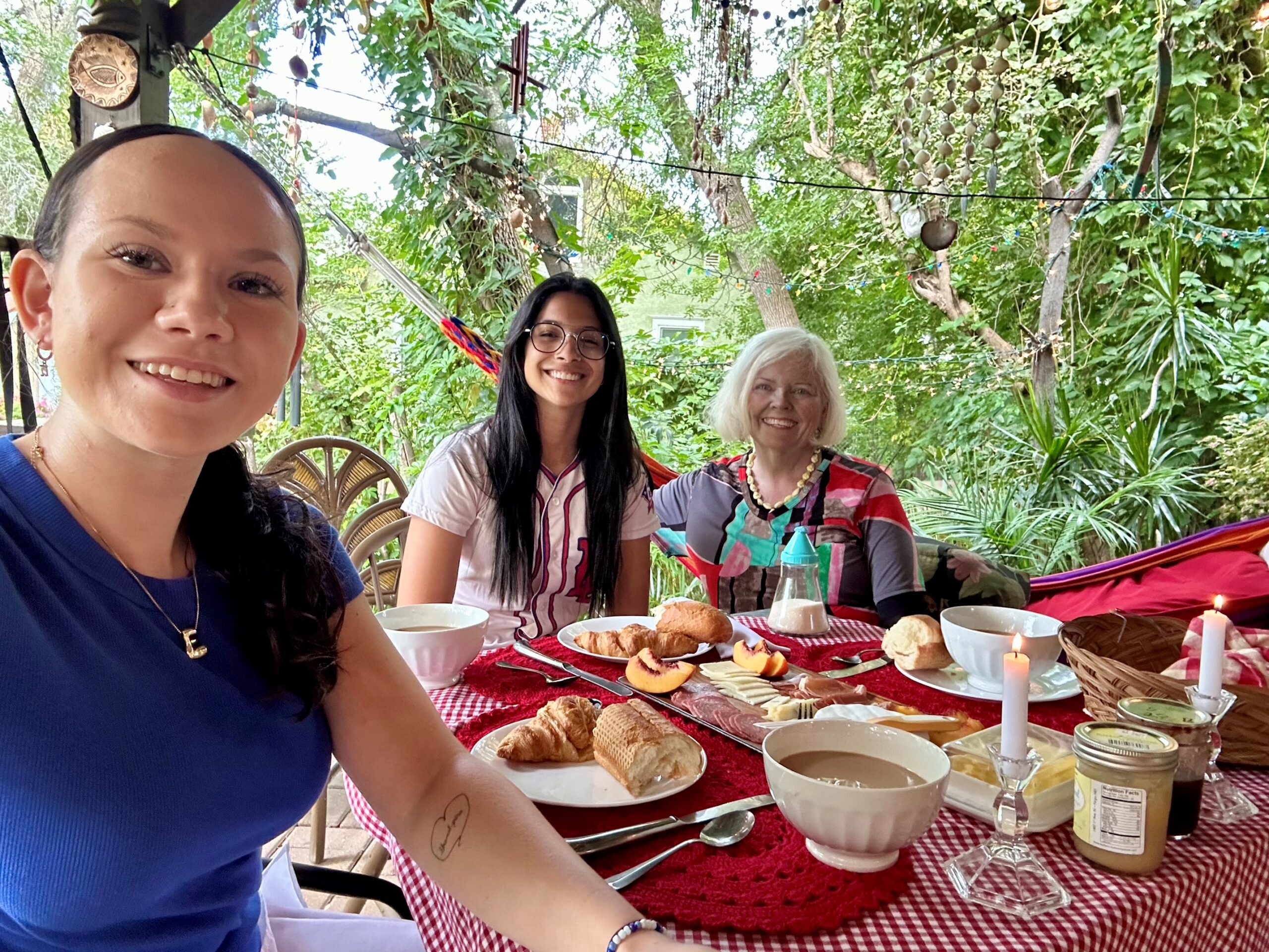Outdoor breakfast gathering. Three individuals enjoy a meal on a patio surrounded by greenery.