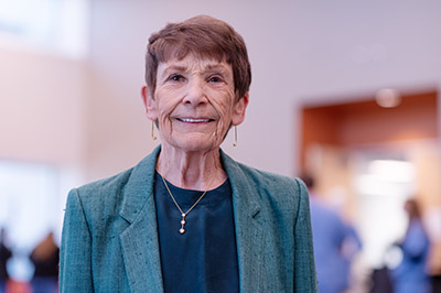 Portrait of a woman with brown hair, a green jacket and blouse, and a gold necklace. 