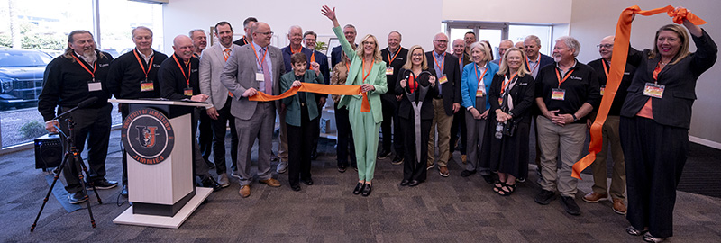 A group of people hold a chopped ribbon and a large pair of scissors at the opening of a facility. 