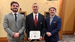 Three men standing together, one has an award.
