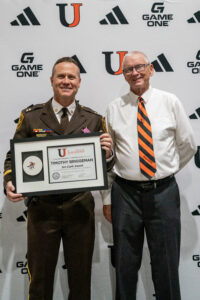Two men pose for photo. One is holding an award.