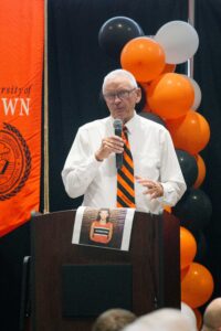 man with orange and black tie on stage with microphone