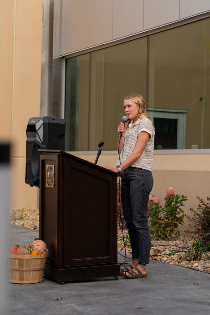 Young woman stands at outdoor podium, delivering a speech
