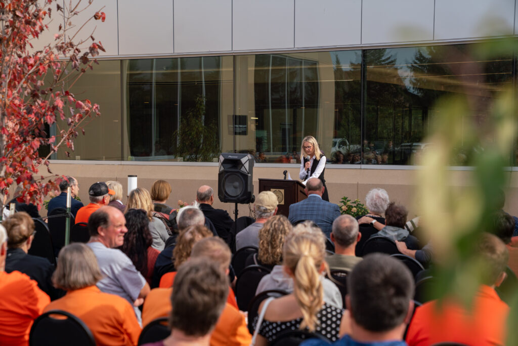 Woman stands at podium in front of a building, giving speech to a crowd